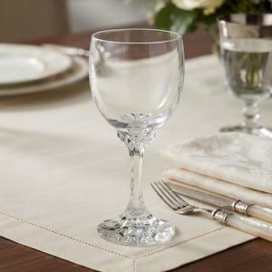 Può includere: Un calice da vino in vetro trasparente con una coppa liscia e arrotondata e uno stelo in vetro molato sfaccettato che si apre in una base con motivo a stella. Lo stelo presenta dettagli geometrici complessi e una finitura riflettente.