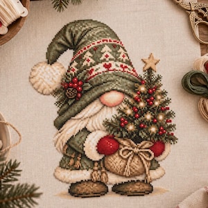 May include: A cross-stitch embroidery on beige fabric featuring a gnome wearing a green hat with white tree patterns and a red heart border. The gnome has a long white beard, red mittens, and holds a small Christmas tree with red berries.