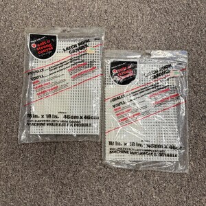 May include: Two packages of white Red Heart Soft & Strong latch hook canvas. Each clear plastic bag contains a 18 in. x 18 in. square of polyester mesh fabric. The packaging features black and red text detailing the product features and dimensions.