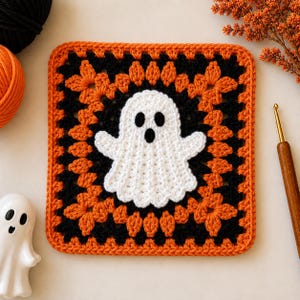 Può includere: Un quadrato all'uncinetto di tipo granny square che presenta un fantasma bianco centrale con occhi e bocca neri. Il fantasma è circondato da giri alternati di filato nero e arancione in un motivo classico con un bordo arancione solido.