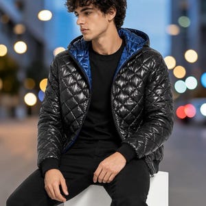 May include: A black quilted puffer jacket with a shiny finish, featuring a hood with a contrasting bright blue interior lining, a front zipper closure, and black ribbed cuffs, worn over a plain black t-shirt and black pants.