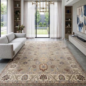 May include: A large rectangular area rug featuring a traditional floral and vine pattern in shades of beige, brown, blue, and cream. The rug has a wide decorative border with intricate motifs and short white fringe along the short edges.