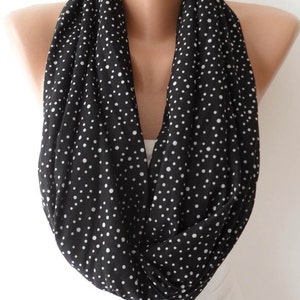 May include: Black infinity scarf with white polka dots. The scarf is draped around a mannequin's neck, showcasing its circular design. The fabric appears soft and lightweight, suitable for various seasons. A classic accessory.
