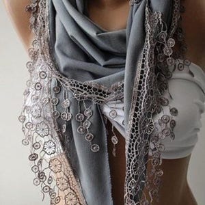 May include: A grey scarf with a delicate lace trim. The lace has a floral pattern and hangs in long fringes.