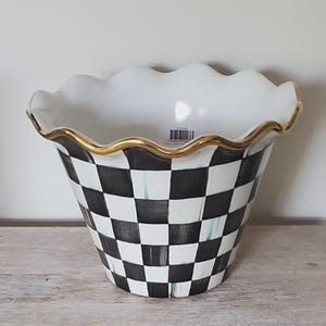May include: A ceramic planter featuring a black and white checkered pattern on the exterior. The vessel has a wide, scalloped rim finished with a thin gold-tone metallic trim. A small barcode sticker is visible on the interior white surface.