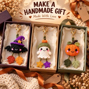 Könnte beinhalten: Drei Häkel-Schlüsselanhänger in einzelnen Geschenkboxen. Einer ist eine schwarze Fledermaus mit violettem Hexenhut und orange-gelben Blattfüßen. Ein weißes Gespenst mit grünem Hut und gelb-violetten Sternfüßen. Ein orangefarbener Kürbis mit Blattfüßen.
