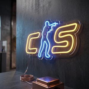 以下が含まれることがあります： 黄色い文字のCとS、その間にライフルを構える人物の青いシルエットが描かれたネオンサイン。シルエットの中には青い文字でNEONと縦書きされている。このサインは暗い壁に取り付けられている。