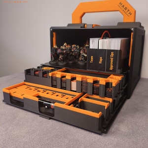 Può includere: Una custodia modulare grigio scuro e arancione con maniglia superiore e logo Harth Lines. L'interno contiene scomparti organizzati con miniature e mazzi di carte con le etichette Team, Maps e Approved Ops.