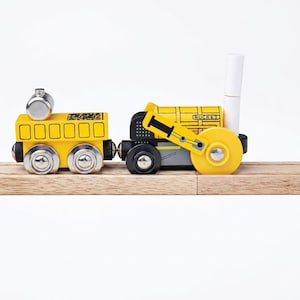 May include: A wooden toy train set consisting of a yellow carriage with a silver top piece and a black and yellow locomotive engine labelled ROCKET with a white vertical chimney, both resting on a wooden track section against a white background.