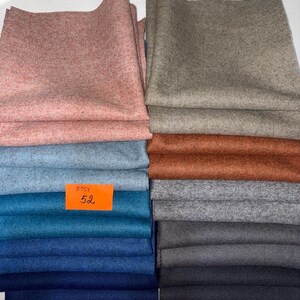 May include: A collection of folded fabric swatches in various colours including pink, light blue, teal, dark blue, beige, rust, grey, and charcoal. An orange rectangular tag with the black text ETSY 52 is placed on the blue fabric stack.