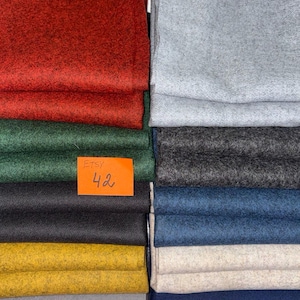 May include: A collection of folded fabric pieces in various solid colours including red, dark green, black, yellow, light grey, light blue, charcoal grey, blue, beige, and navy blue. An orange rectangular tag with the handwritten text ETSY 42 is visible.