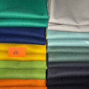May include: A collection of folded fabric swatches in various colours including emerald green, navy blue, mustard yellow, lime green, orange, light grey, sage green, dark grey, and black. An orange rectangular tag with the text ETSY 50 is visible.