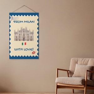 Può includere: Un arazzo rettangolare disegnato come un francobollo con sfondo color crema e bordo blu smerlato. Presenta un'illustrazione del Duomo di Milano, il testo FROM MILAN WITH LOVE!, una bandiera italiana e un'impronta di labbra rosse.