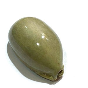 May include: A smooth, olive-green ceramic object with a rounded, elongated shape and a glossy finish. The piece features a small, recessed opening at one end, showcasing a solid, uniform colour throughout its curved, polished surface.