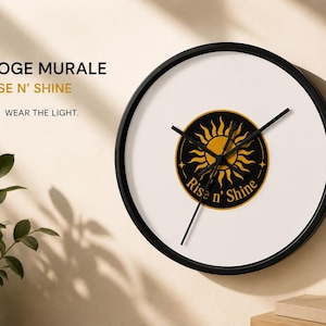 Puede incluir: Un reloj de pared redondo con marco negro y esfera blanca. El centro presenta un emblema circular negro con un gr&aacute;fico de sol dorado y el texto Rise n' Shine. El reloj tiene tres manecillas negras y se muestra con el texto 01 HORLOGE MURALE RISE N' SHINE WEAR THE LIGHT.