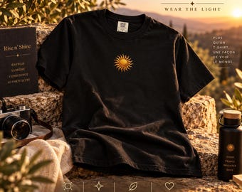 Puede incluir: Una camiseta negra de manga corta con un pequeño gráfico de sol dorado bordado en el centro del pecho. La prenda tiene cuello redondo y un corte estándar. La etiqueta interior del cuello muestra la marca Comfort Colors y la talla L.