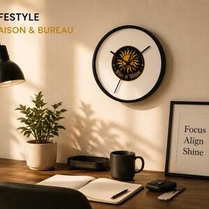 Puede incluir: Un reloj de pared redondo con esfera blanca y marco negro, que presenta un gr&aacute;fico de sol amarillo central con el texto "Rise n' Shine" en negro. El reloj tiene tres manecillas negras delgadas y est&aacute; montado en una pared sobre un escritorio.