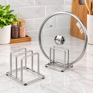 May include: Two silver-toned metal kitchen organizers with a rectangular base and three vertical wire dividers. One organizer is empty, while the other holds a circular glass pot lid with a silver metal handle and a small steam vent hole.