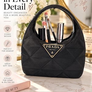 Könnte beinhalten: Ein schwarzer, gesteppter Beauty-Organizer in Handtaschenform mit einer dreieckigen, goldenen Prada Milano Logo-Plakette auf der Vorderseite. Die Tasche enthält mehrere Make-up-Pinsel und Kosmetiktuben. Der Text auf dem Bild umfasst Luxury in Every Detail, Organize Your Beauty In Style, Iconic Design, Perfect for Makeup, Great Gift Idea, Stylish for Home & On the Go, Beauty, Shop Now on Etsy und A little luxury every day.