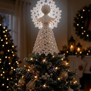 May include: A white crocheted angel tree topper featuring a circular halo with intricate lace-like patterns and a flared, textured dress. The figure is illuminated from behind, casting a soft glow through the openwork stitches of the design.