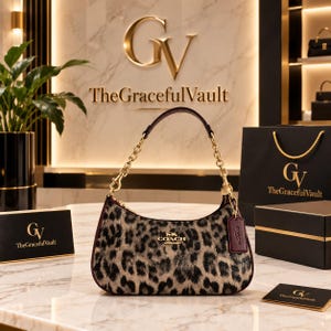 Könnte beinhalten: Eine Coach Hobo-Tasche mit beigem und schwarzem Leopardenmuster, einem goldfarbenen Kettenriemen und einem dunkelroten Lederanhänger. Die Tasche hat einen goldfarbenen Reißverschluss und ein kleines goldenes Coach-Logo auf der Vorderseite.