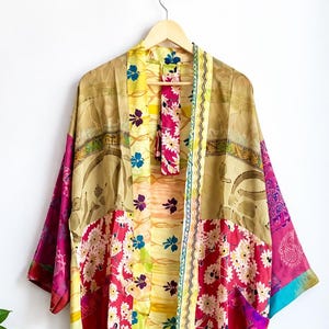 Op de afbeelding: Een kimono met lange mouwen voorzien van een patchworkontwerp met diverse bloemenpatronen in tinten roze, geel, goud en blauw. Het kledingstuk heeft een open voorzijde, wijde mouwen en een constructie van lichtgewicht stof.