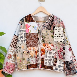 Peut inclure: Une veste matelassée à manches longues présentant un motif patchwork avec divers imprimés floraux, cachemire et éléphants dans des tons de marron, beige, rose et blanc. La veste possède un col en V, une fermeture boutonnée et deux poches carrées.