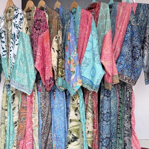 May include: A collection of long, open-front robes hanging on a white rack. Each robe features a unique combination of vibrant colors and intricate patterns, including paisley, floral, and abstract designs in shades of blue, pink, green, and gold.