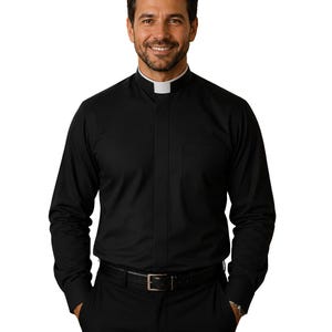 May include: A long-sleeved black clergy shirt featuring a white tab collar insert, a concealed button placket, and a single chest pocket. The shirt is paired with black trousers and a black leather belt with a silver-toned metal buckle.
