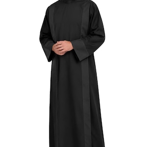 May include: A black cassock featuring a high collar, long sleeves with wide cuffs, and vertical panels running down the front. The garment is floor-length and constructed from a solid black fabric with a matte finish, providing a structured appearance.