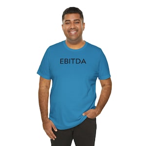 May include: A bright blue short-sleeved t-shirt featuring the word EBITDA printed in bold black capital letters across the center of the chest. The garment has a classic crew neckline and a standard fit, providing a simple and clean appearance.