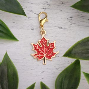 Peut inclure: Une breloque en métal doré en forme de feuille d'érable avec un remplissage en émail rouge vif. La breloque est dotée d'un fermoir mousqueton doré fixé sur le dessus, ce qui permet de l'accrocher facilement à divers objets décoratifs.