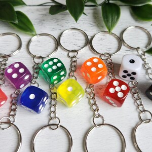May include: A selection of dice keyrings in various colours. Each die is a different colour, including red, purple, green, yellow, orange, blue, white, and black. The dice have white spots and are attached to silver keyrings.
