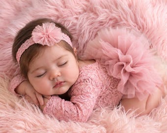 May include: A dusty pink long-sleeved lace romper featuring a layered tulle tutu skirt attached at the waist, paired with a matching elastic headband adorned with a small, circular, ruffled fabric flower accent in the same shade of pink.
