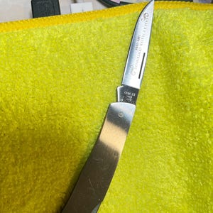 Könnte beinhalten: Ein Klappmesser aus Edelstahl mit silberner Klinge und poliertem Griff. Die Klinge ist mit dem Text "CASE XX TESTED CENTENNIAL 1889-1989" graviert. Das Messer ist teilweise geöffnet und zeigt die scharfe Kante.