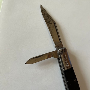 May include: A black handled pocket knife with two blades. The knife is open and the blade is visible. The knife has the words "Barlow" and "Camco" on the handle.