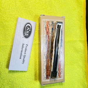 May include: A folding pocket knife in a rectangular tan box with a red, white, and blue flag pattern, featuring the text WWW.WRCASE.COM. Beside the box is a white informational pamphlet with the Case XX logo and the text Product Quality Information.