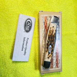 May include: A folding pocket knife with a textured brown and cream handle, featuring silver bolsters and a Case logo inlay, resting in a rectangular box with an American flag design, accompanied by a white Case product information pamphlet.
