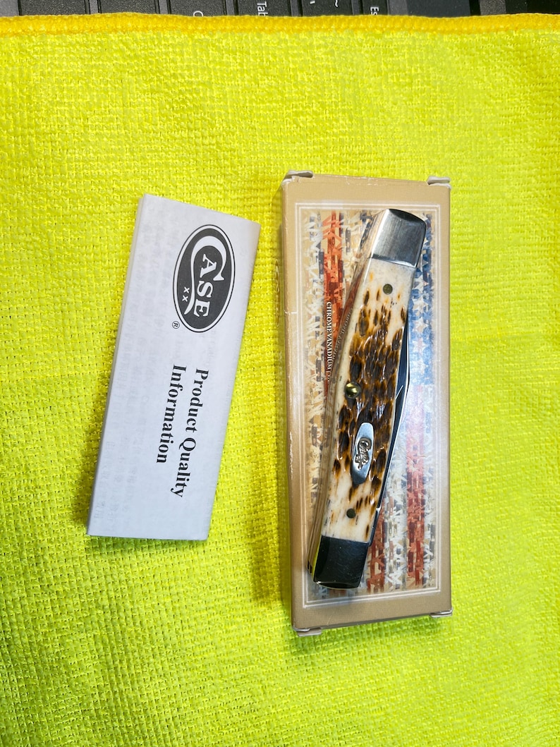 May include: A folding pocket knife with a textured brown and cream handle, featuring silver bolsters and a Case logo inlay, resting in a rectangular box with an American flag design, accompanied by a white Case product information pamphlet.