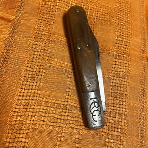 Puede incluir: Un cuchillo de bolsillo marrón con mango de madera y hoja de metal. El cuchillo tiene una inscripción de metal que dice "R.R.C."