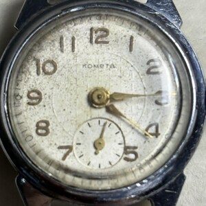 May include: A vintage silver-tone wristwatch with a textured off-white dial featuring the Cyrillic text "KOMETA" below the twelve o'clock position. The watch has gold-tone hands, Arabic numerals, and a small sub-dial for seconds at the bottom.