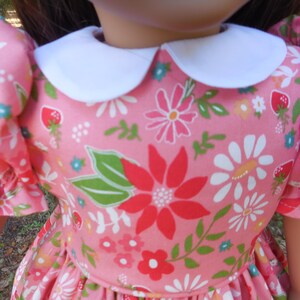 May include: A pink doll dress with a white collar and floral pattern. The dress features a print of red, white, and pink flowers, green leaves, and strawberries. The sleeves are short and puffed.