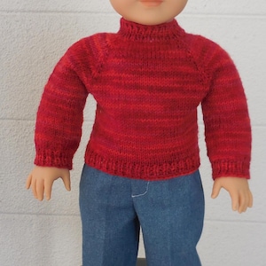 May include: A doll wearing a red knit sweater and blue jeans. The sweater has a ribbed texture and long sleeves. The doll is also wearing white sneakers with red accents. The doll has light brown hair and is standing in front of a white wall.