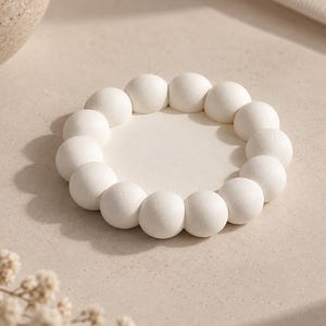May include: A circular white tray featuring a raised border composed of numerous small, smooth spheres arranged in a continuous ring. The center of the tray is flat and smooth, providing a consistent matte finish across the entire object.