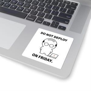 May include: A square white sticker featuring a black line drawing of a bald character wearing round glasses, standing next to a laptop with a red warning triangle on the screen. The text DO NOT DEPLOY ON FRIDAY is printed in black capital letters.