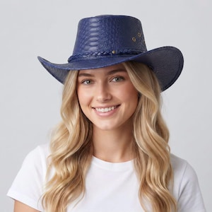 Pode incluir: Um chapéu de cowboy azul-marinho com um padrão texturizado de pele de cobra na copa e na aba. O chapéu inclui uma faixa trançada ao redor da base e pequenos ilhós metálicos na lateral para ventilação.