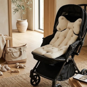May include: A black stroller featuring a cream-colored, tufted seat liner with a subtle, repeating pattern of small brown bear icons. The stroller includes a matching head support cushion, a black canopy, and a storage basket located underneath the seat.