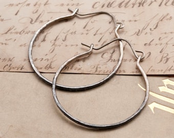 May include: A pair of silver hoop earrings with a hammered texture. The earrings are on a vintage book with handwritten text.
