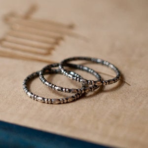 May include: Four silver rings with a beaded design stacked on top of each other on a brown surface.