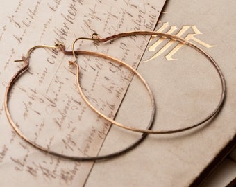 May include: A pair of gold hoop earrings on a vintage book with handwritten text. The earrings are simple and elegant, with a smooth, polished finish.